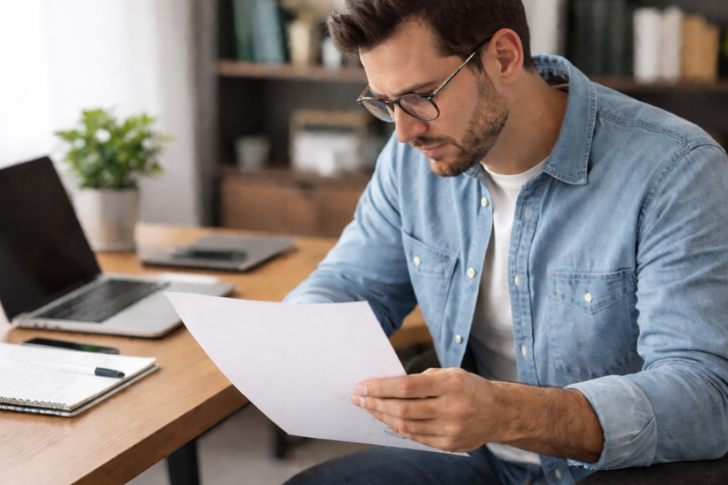 Mann sitzt am Schreibtisch und prüft ein leeres Dokument im Zusammenhang mit einer SCHUFA-Selbstauskunft
