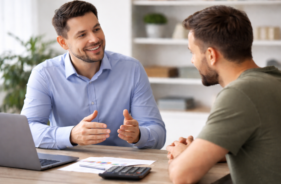 Zwei Männer im Gespräch an einem Tisch in modernem Büro, sachliche Beratungssituation im Finanzkontext