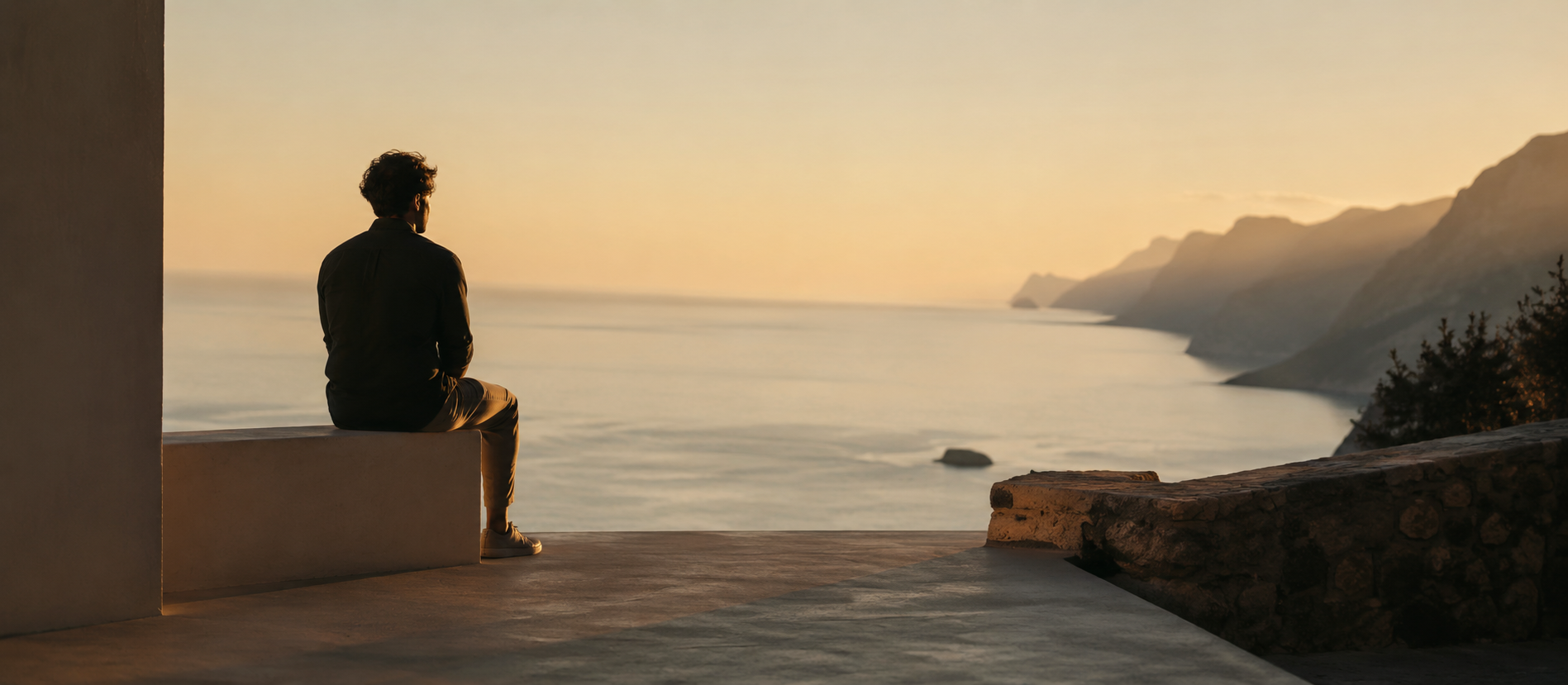 Alleinreisender Mann auf ruhiger Terrasse mit weitem Blick über das Meer bei warmem Sonnenuntergang, minimalistische Architektur, friedliche Atmosphäre, cineastisches Licht, reflektierende Stimmung nach einer Trennung, viel Freiraum und natürliche warme Farbtöne im Editorial-Stil.