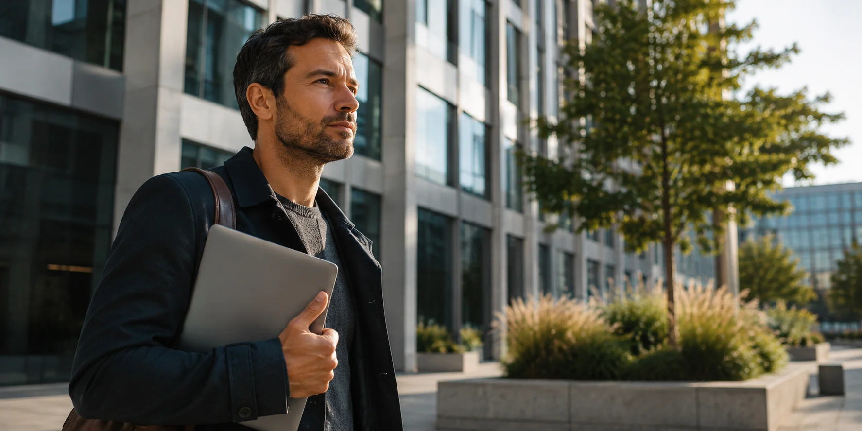 Ein Mann mit Laptop steht vor modernen Bürogebäuden und blickt entschlossen in die Ferne. Das Bild verdeutlicht das Thema Kredit mit befristetem Arbeitsvertrag und die Bedeutung einer stabilen beruflichen Perspektive für die Kreditentscheidung von Banken.
